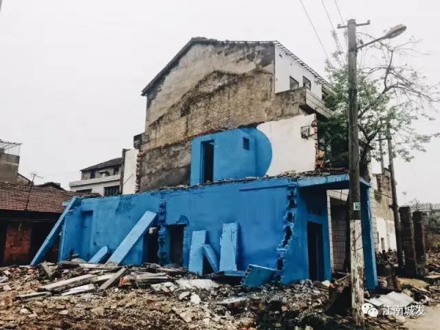 △ 這棟建筑是臨江最近的半拆遷建筑物的遺留，沅江和堤壩成為了展覽的天然背景。創(chuàng)作團(tuán)隊對這棟建筑進(jìn)行了半涂裝，將符號性的沅水曲線與拆遷進(jìn)行中的建筑立面進(jìn)行意義的疊造，它們共同觸發(fā)了場所空間多元語境的生成，把拆遷這種暫時破壞性、干擾性的介入行動與沅水右岸發(fā)展的未來性、美好性緊密融合。